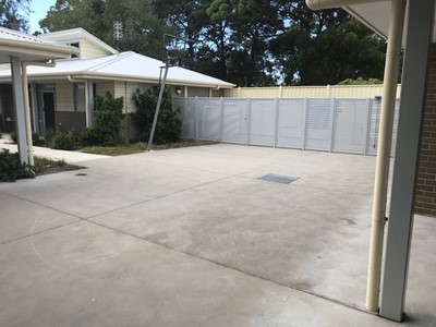 Outdoor area in self-contained unit in Lifestyle Solutions Specialist Disability Accommodation in Argenton, Newcastle, NSW showing secure fencing between properties, showing fully accessible front door, garage and bin area