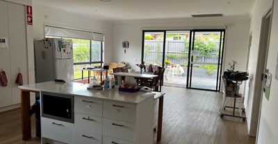 Accessible kitchen and dining area leading to outdoor verandah and covered dining area in Lifestyle Solutions three-bedroom Specialist Disability Accommodation (SDA) in Pallara, Qld