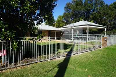Front of Lifestyle Solutions Supported Independent Living property in Wyong, NSW, showing full fencing and trees for privacy